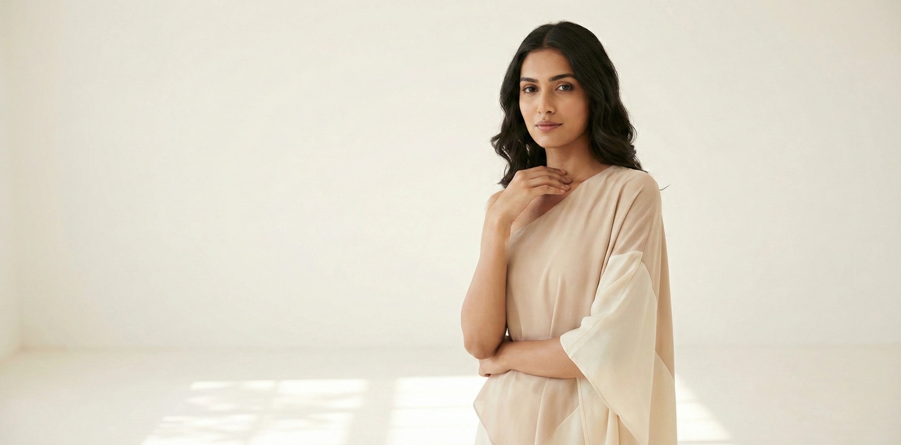 Female model wearing a SwanClad beige one-shoulder minimalist dress with a modern drape, posed in a clean studio environment.