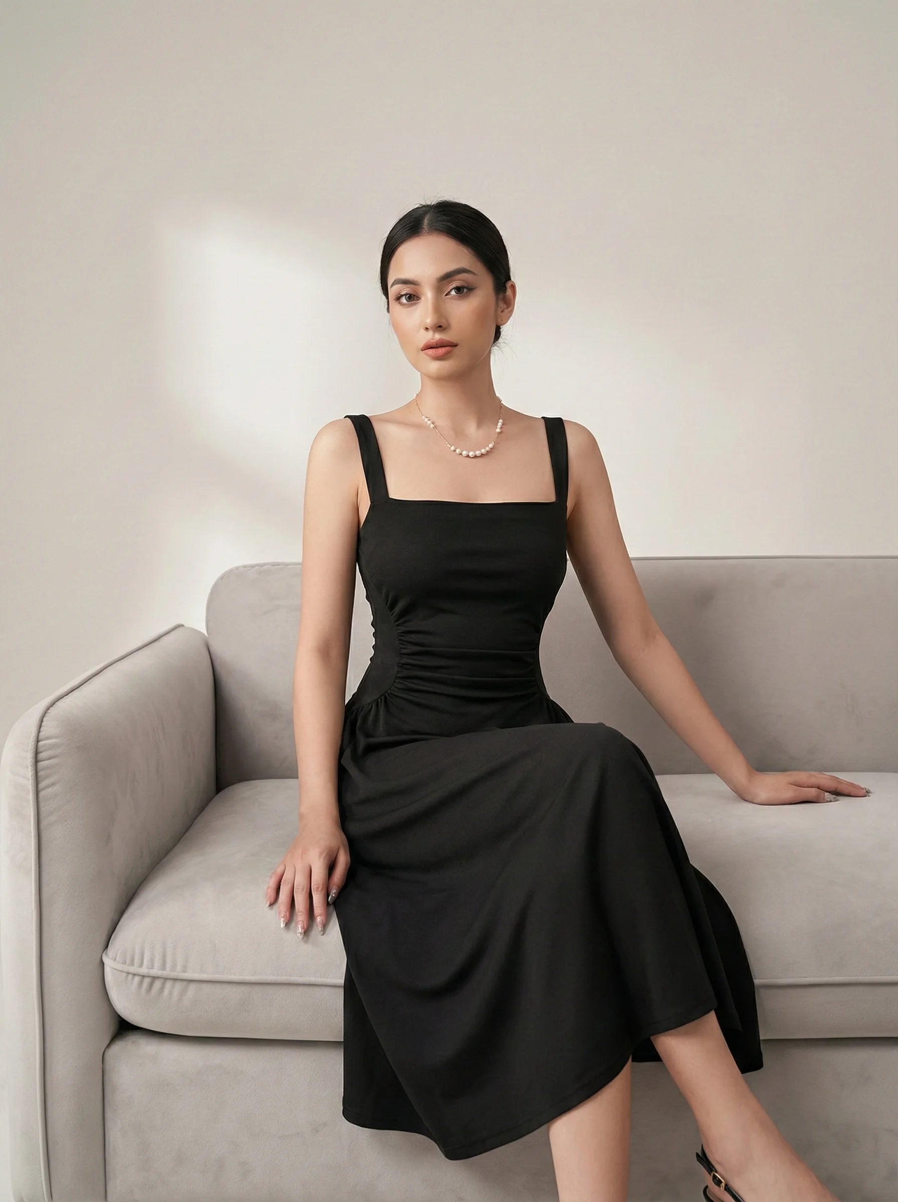 SwanClad Black Shoulder Strapped Ruched Fit And Flare Midi Dress styled in elegant sitting pose on sofa in minimal studio