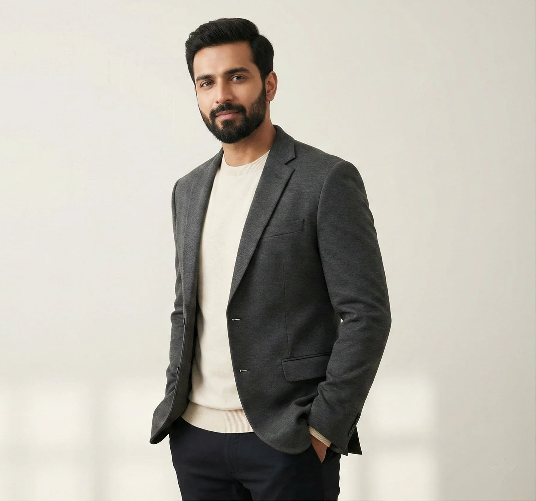 Men wearing a grey tailored blazer over a cream sweater, styled in a minimalist studio setting by SwanClad.