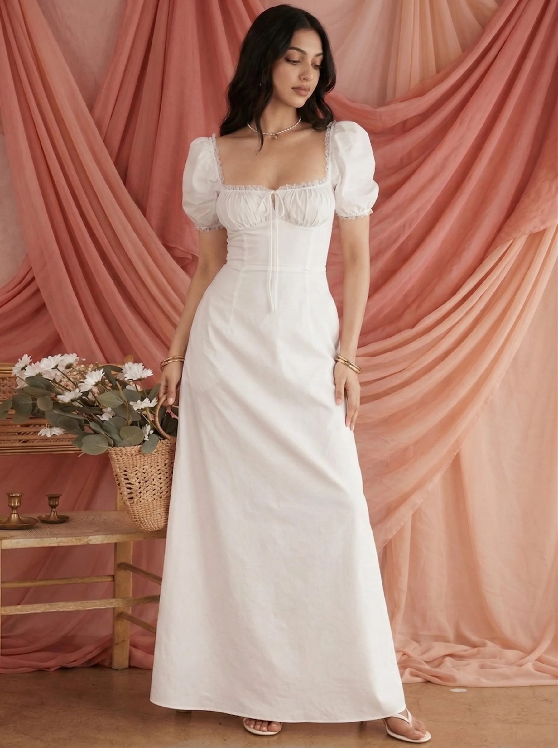 Elegant white puff sleeve maxi dress for women by SwanClad, featuring a square neckline and flowy silhouette against a soft peach draped backdrop.