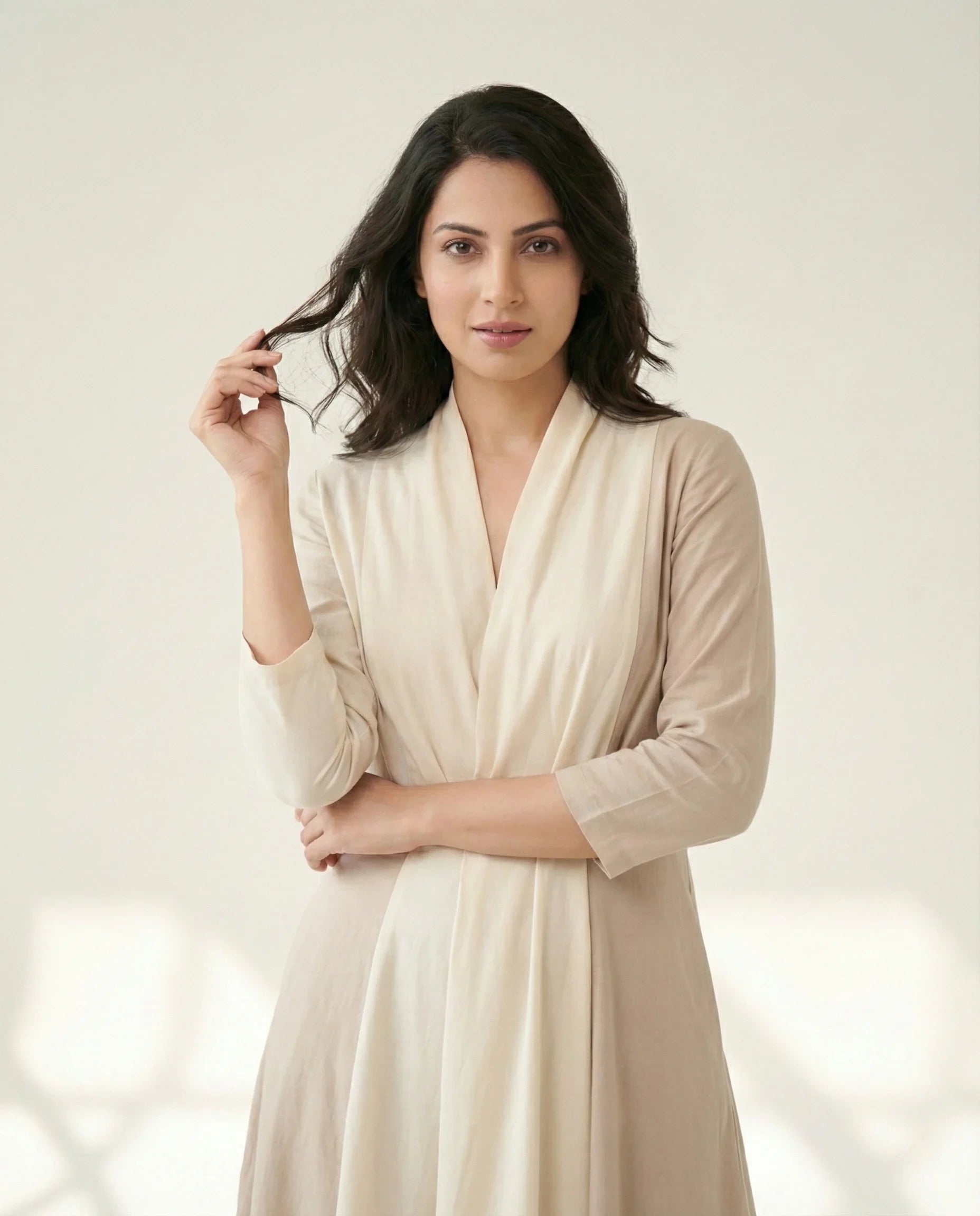 Female model wearing a SwanClad cream wrap dress with soft drape and three-quarter sleeves, photographed against a neutral studio background.