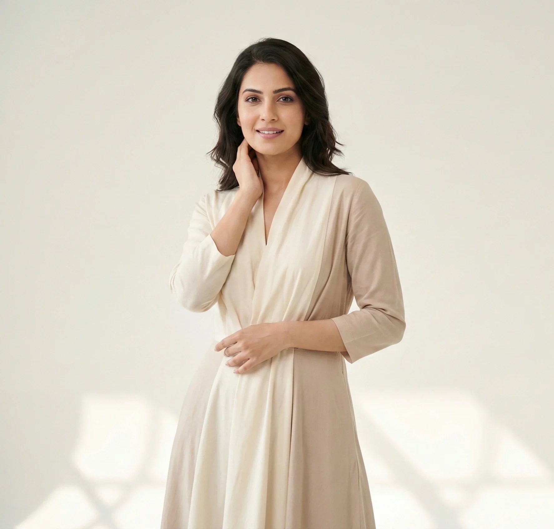 Woman modeling a SwanClad cream wrap dress with a flowy silhouette and minimal detailing, styled in soft natural studio lighting.
